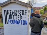The group painting 'Newcastle United Foundation' on the allotment wall 