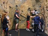 The group are doing indoor rock climbing, climbing the hall and holding each others ropes 